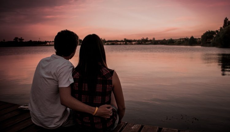 בחור ובחורה יושבים מול הים והגבר מחבק אותה בידו הימנית