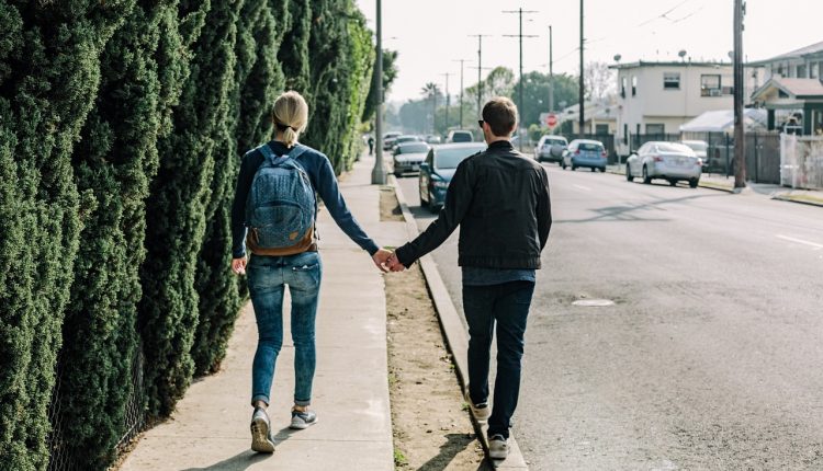 זוג הולך יחד יד ביד במדרכה לצד הכביש